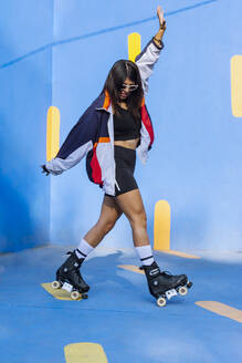 Woman wearing roller skates dancing by wall - EGCF00007