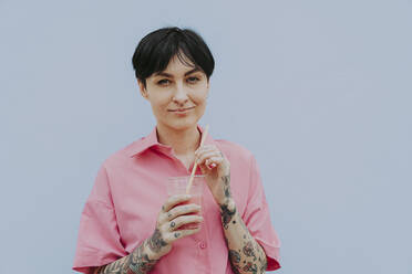 Smiling woman holding glass standing in front of gray wall - OIPF02338