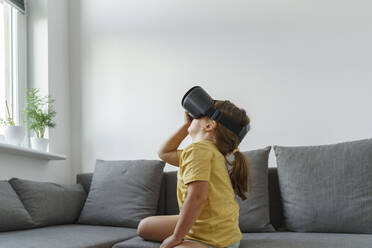 Girl wearing VR glasses sitting on sofa in living room - TOF00005