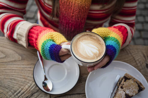 Hands of woman wearing rainbow gloves holding coffee cup at table - OSF00720
