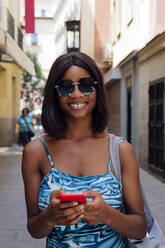 Glückliche Frau mit Sonnenbrille und Mobiltelefon - PGF01156