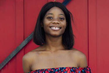 Lächelnde junge Frau vor einer roten Tür - PGF01167