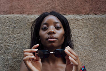 Junge Frau mit Sonnenbrille vor einer Mauer - PGF01187