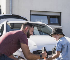 Father and son charging electric car in front of residential house - UUF27076