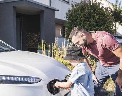 Vater und Sohn laden ein Elektroauto vor einem Wohnhaus auf - UUF27077