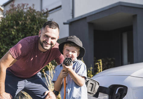 Vater und Sohn laden ein Elektroauto vor einem Wohnhaus auf - UUF27082