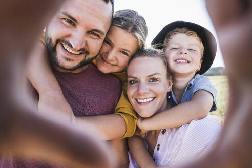 Laughing family embracing and looking through hands at camera - UUF27101