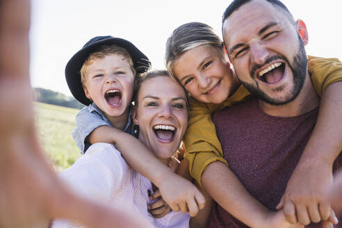 Laughing family embracing and looking through hands at camera - UUF27103