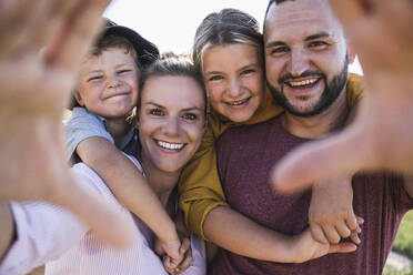 Lachende Familie, die sich umarmt und durch die Hände in die Kamera schaut - UUF27104