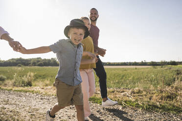 Happy boy holding hands of family walking through nature - UUF27108