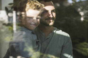 Vater hält seinen Sohn auf dem Arm und schaut durch ein Fenster - UUF27109