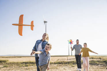 Glückliche Familie spaziert durch den Windpark Kinder tragen Spielzeug - UUF27110