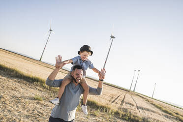 Father carrying son on shoulders in front of wind turbines - UUF27128