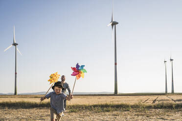 Junge mit bunten Windrädern läuft im Windpark mit Vater hinterher - UUF27130