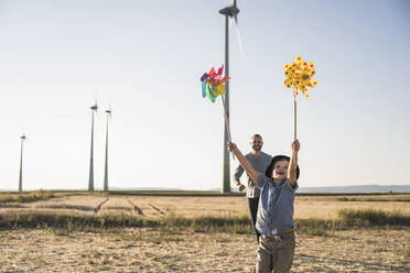 Junge mit bunten Windrädern läuft im Windpark mit Vater hinterher - UUF27131