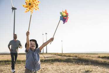 Junge mit bunten Windrädern läuft im Windpark mit Vater hinterher - UUF27132