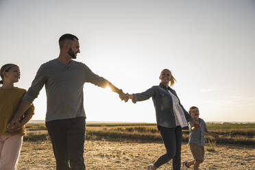 Selbstbewusste Familie, die sich bei Sonnenuntergang an den Händen hält - UUF27137