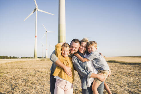 Happy family standing in wind park embracing children - UUF27143