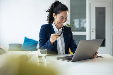 Glückliche Geschäftsfrau mit Kreditkarte beim Online-Einkauf über einen Laptop zu Hause - JOSEF11949