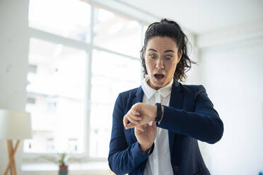 Schockierte Geschäftsfrau mit Blick auf eine intelligente Uhr - JOSEF11954