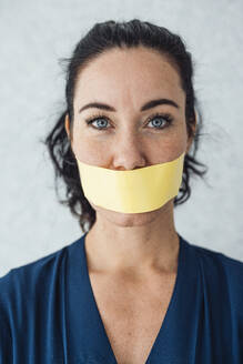 Woman with tape over mouth standing in front of gray wall - JOSEF11980