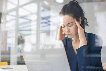 Businesswoman with eyes closed sitting in front of laptop seen through glass - JOSEF11991