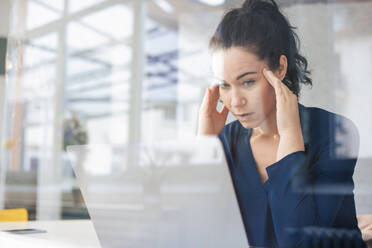 Stressed businesswoman with head in hands looking at laptop - JOSEF11992