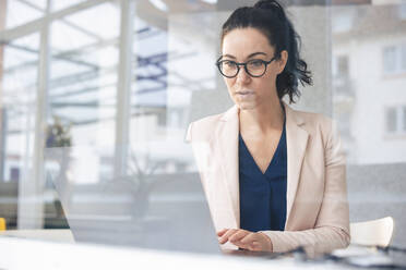 Serious businesswoman working on laptop seen through glass - JOSEF11994