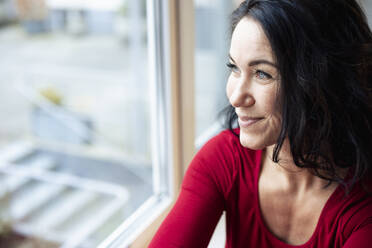 Smiling thoughtful woman looking through window - JOSEF12004
