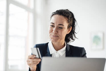 Lächelnde Geschäftsfrau mit Kreditkarte beim Online-Shopping mit dem Laptop zu Hause - JOSEF12021