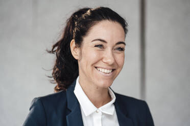 Happy businesswoman in front of gray wall - JOSEF12023