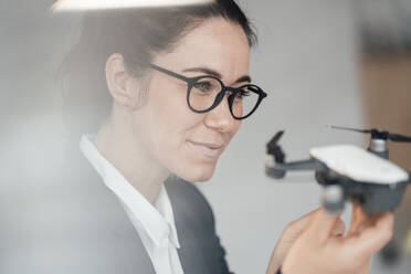 Smiling businesswoman wearing eyeglasses analyzing drone - JOSEF12026