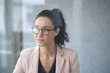 Thoughtful businesswoman wearing eyeglasses in front of wall seen through glass - JOSEF12033