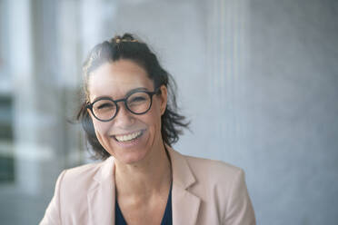 Glückliche Geschäftsfrau mit Brille vor einer grauen Wand durch Glas gesehen - JOSEF12034