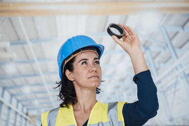 Engineer in reflective clothing looking through ring shape object at factory - JOSEF12042