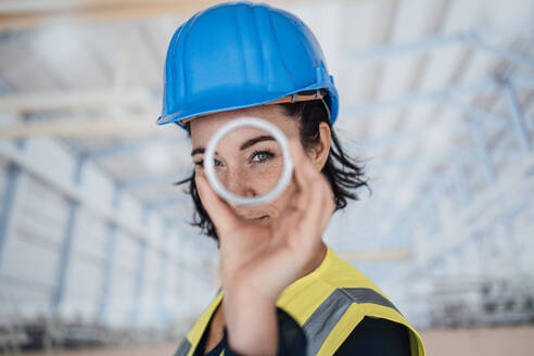 Smiling engineer looking through ring shape object in factory - JOSEF12044