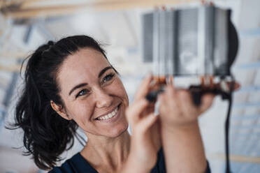 Lächelnde Geschäftsfrau bei der Analyse eines Heizmoduls in einer Fabrik - JOSEF12048