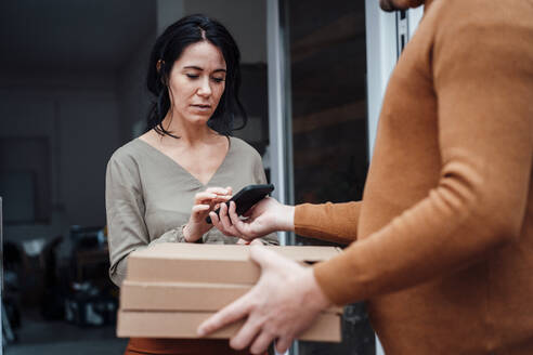 Frau, die ein Paket entgegennimmt und mit ihrem Smartphone an der Haustür unterschreibt - JOSEF12062