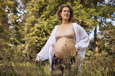 Lächelnde schwangere Frau inmitten von Gras - JHAF00154