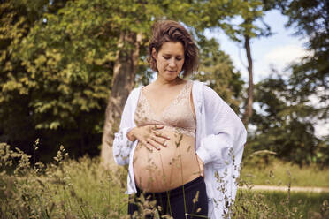 Schwangere Frau mit Händen auf der Hüfte im Gras stehend - JHAF00156