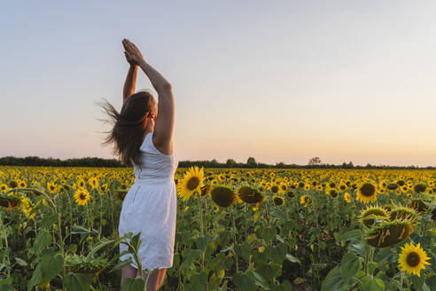 Frau übt Yoga auf einem Sonnenblumenfeld bei Sonnenuntergang - OSF00728