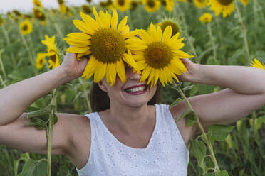 Happy woman covering eyes with sunflowers at field - OSF00733