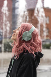 Lächelnde junge Frau mit rosa Haaren hört Musik über Kopfhörer - TOF00023