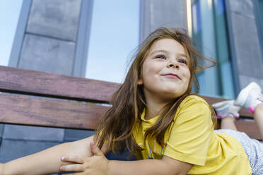 Smiling cute girl with long hair lying on bench - TOF00037