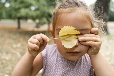 Girl covering eyes with leaf at public park - TOF00044