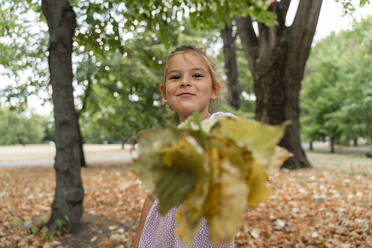 Lächelndes Mädchen mit Blättern im Park stehend - TOF00046