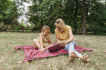 Smiling grandmother with granddaughter using tablet PC at park - TOF00047