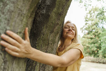 Smiling mature woman hugging tree at park - TOF00055