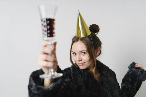 Young woman with wineglass wearing party hat against white background - TOF00070
