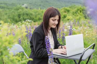 Freiberufler mit Laptop auf dem Schreibtisch, umgeben von Blumen - OSF00737